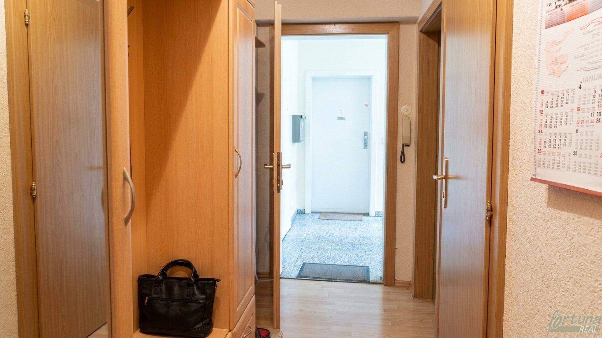 Eingangsbereich mit Holzschrank und Blick in den Flur mit heller Eingangstür.