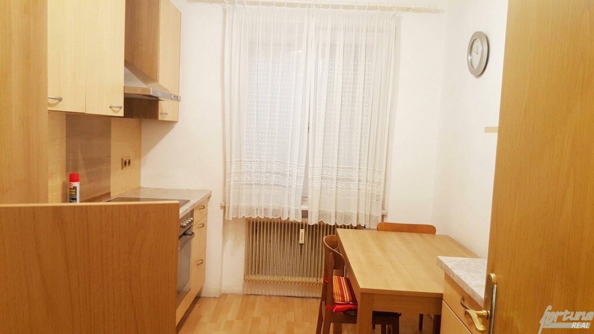Funktionale Küche mit Holzschränken, Esstisch und Fenster mit Blick nach draußen.