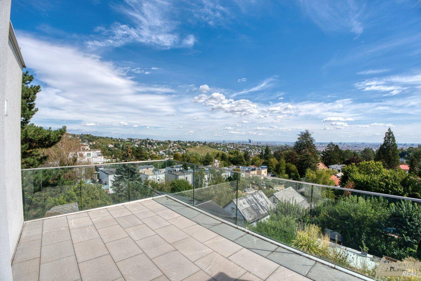 Geräumige Terrasse mit Steinplatten und Glasgeländer bietet einen weiten Blick über die Stadt und Landschaft.