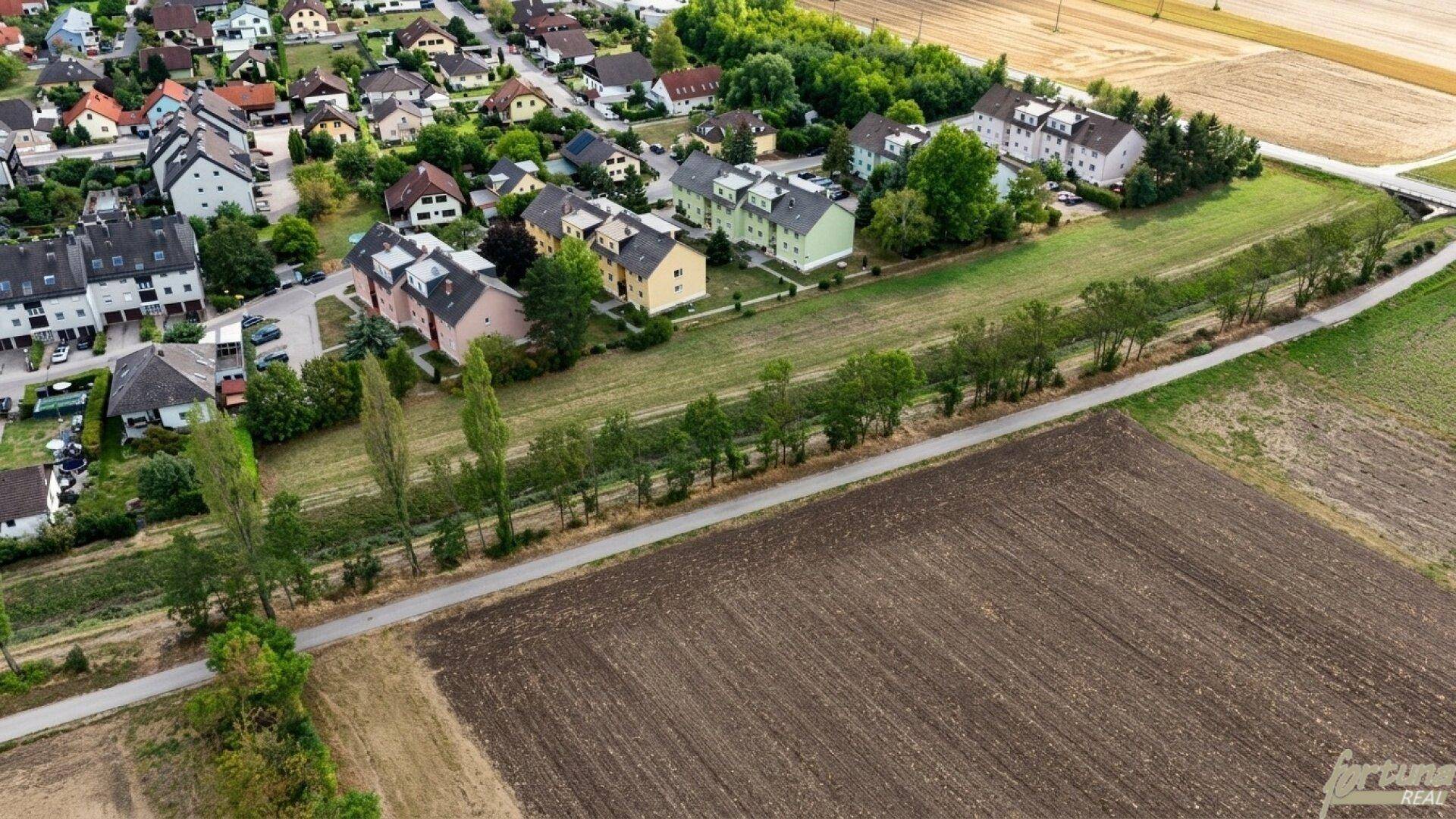 Übersicht einer Wohnsiedlung mit angrenzenden Ackerflächen und einem langen Grünstreifen.