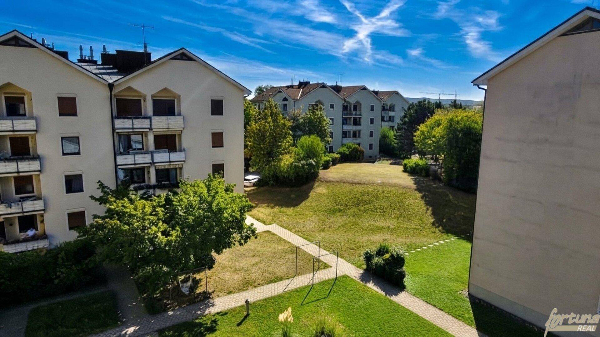 Weitläufiger Blick auf die Wohnanlage mit gepflegtem Gemeinschaftsgarten unter blauem Himmel.