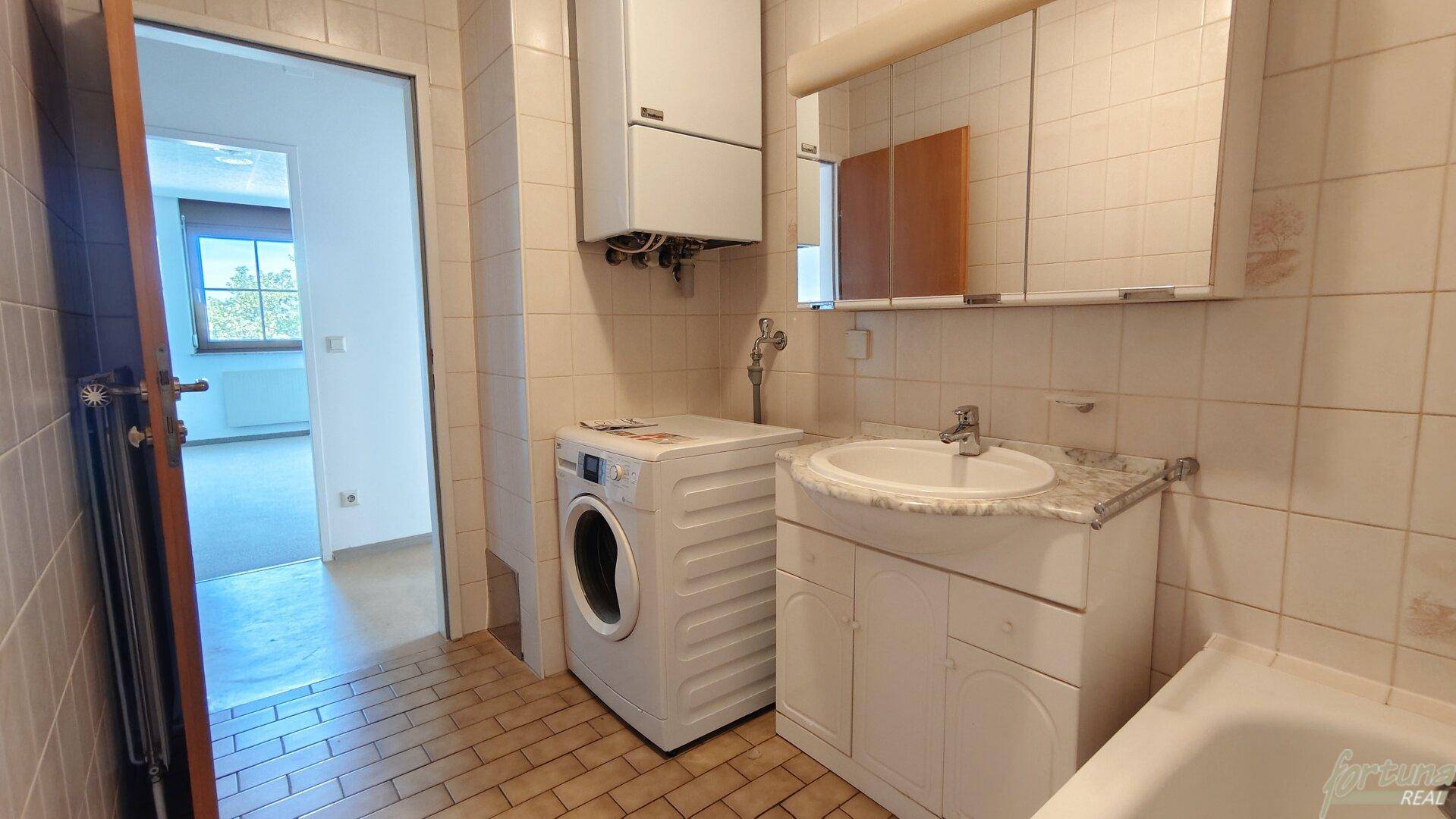 Funktionales Badezimmer mit Fliesenboden, Waschbecken, Badewanne und einer Waschmaschine.