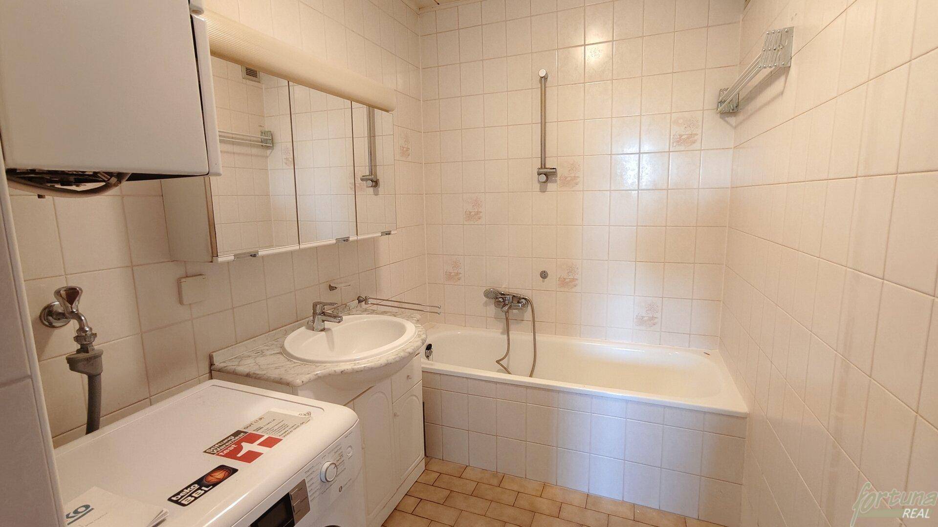 Gefliestes Badezimmer mit Badewanne, Waschbecken und Spiegelschrank, in gutem Zustand.
