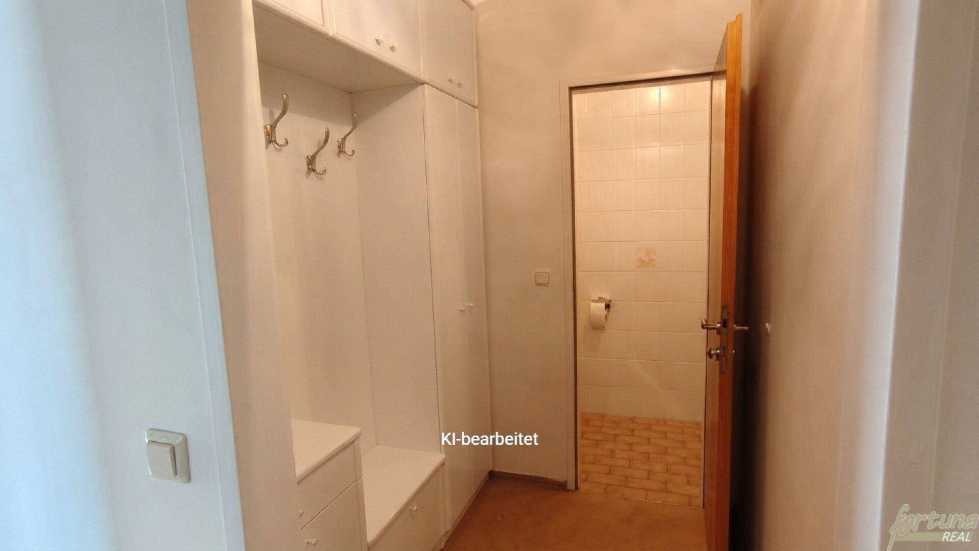 Flur mit weißen Einbauschränken und direktem Zugang zu einem gefliesten WC-Bereich.