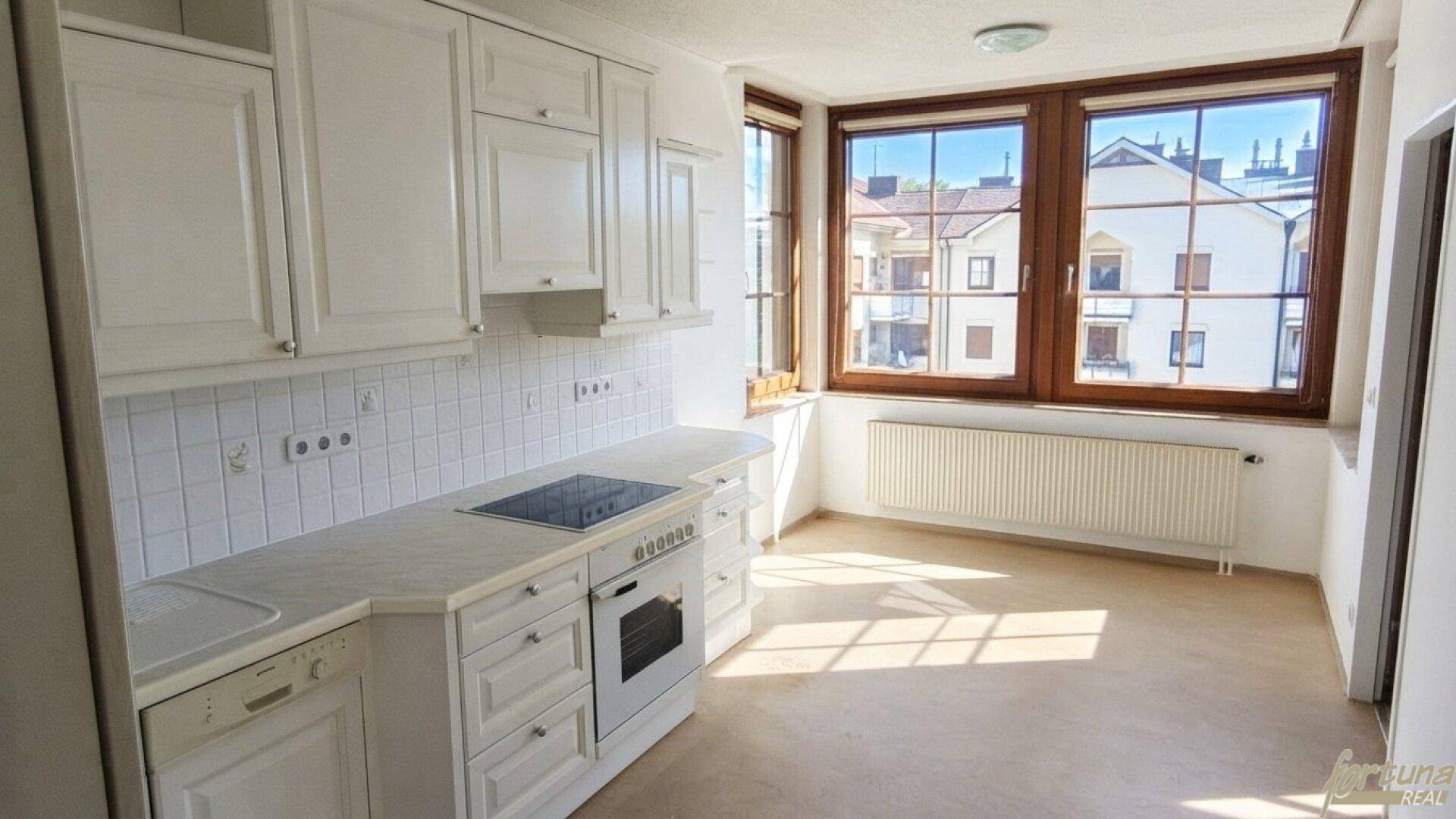 Funktionale Einbauküche mit weißen Schränken, integrierten Geräten und einem hellen Fensterbereich.