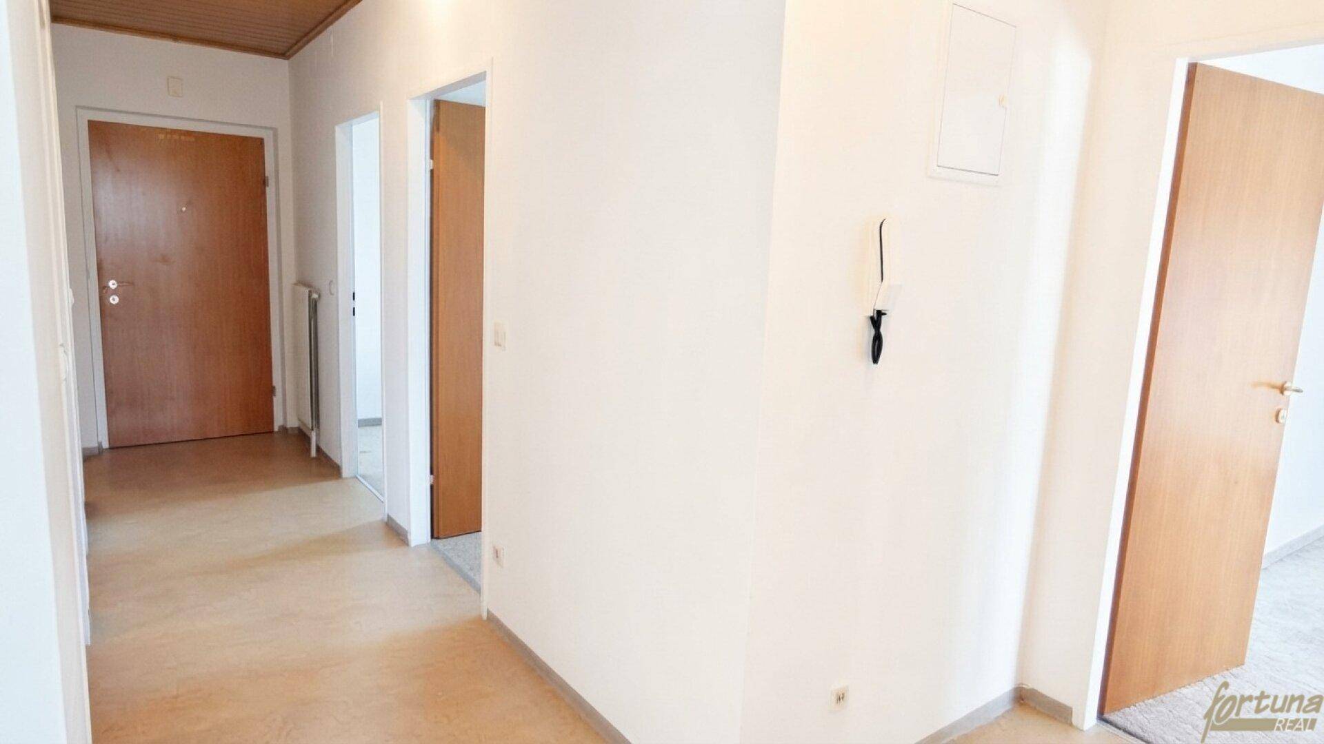Heller Flur mit Holztüren und schlichten weißen Wänden, der zu verschiedenen Räumen führt.