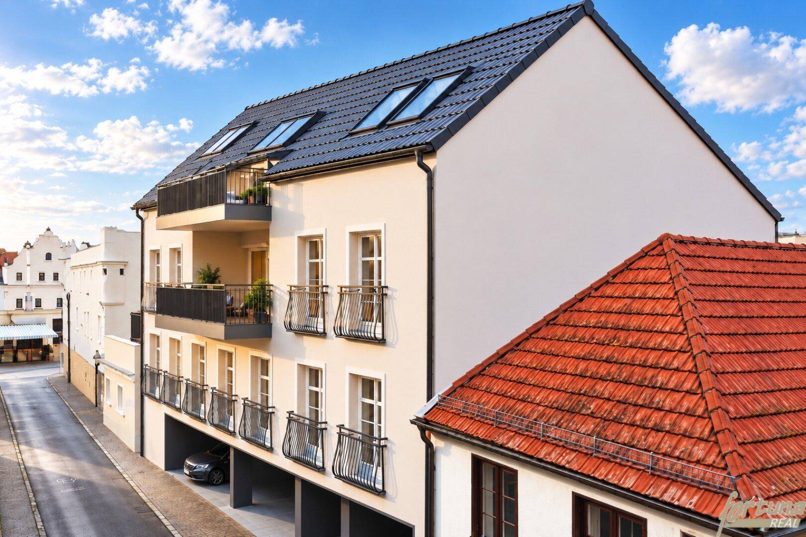 Modernes Mehrfamilienhaus mit dunklem Satteldach, Dachfenstern und Balkonen an einer ruhigen Straße.