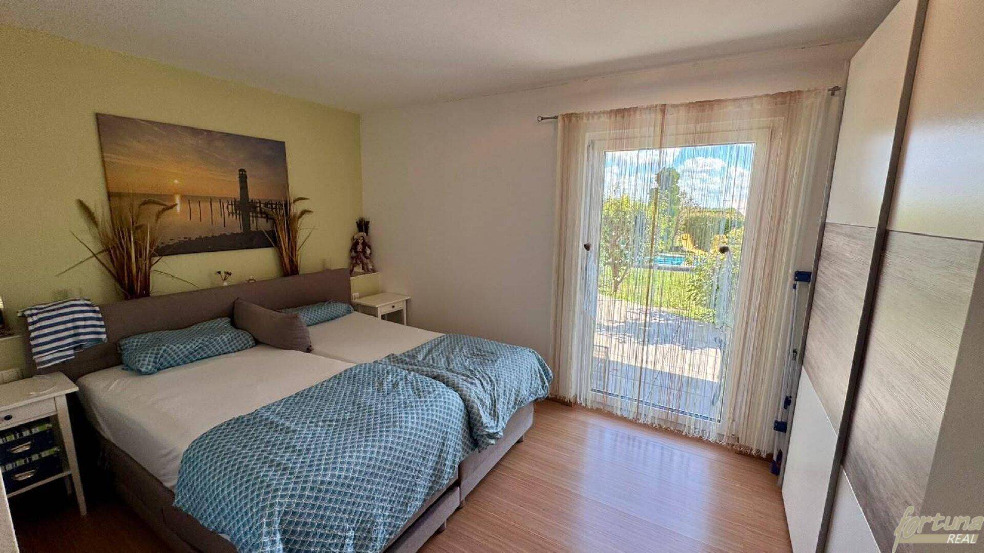 Schlafzimmer mit Doppelbett, Kleiderschrank und direktem Zugang zum Garten und Poolbereich.