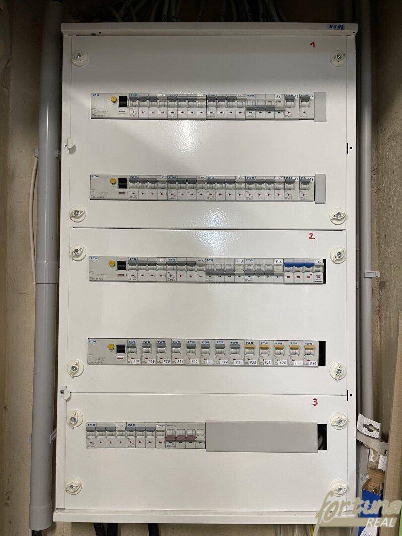 Weißer Elektroschaltkasten mit mehreren Sicherungen und Schaltern, ordentlich an der Wand montiert.
