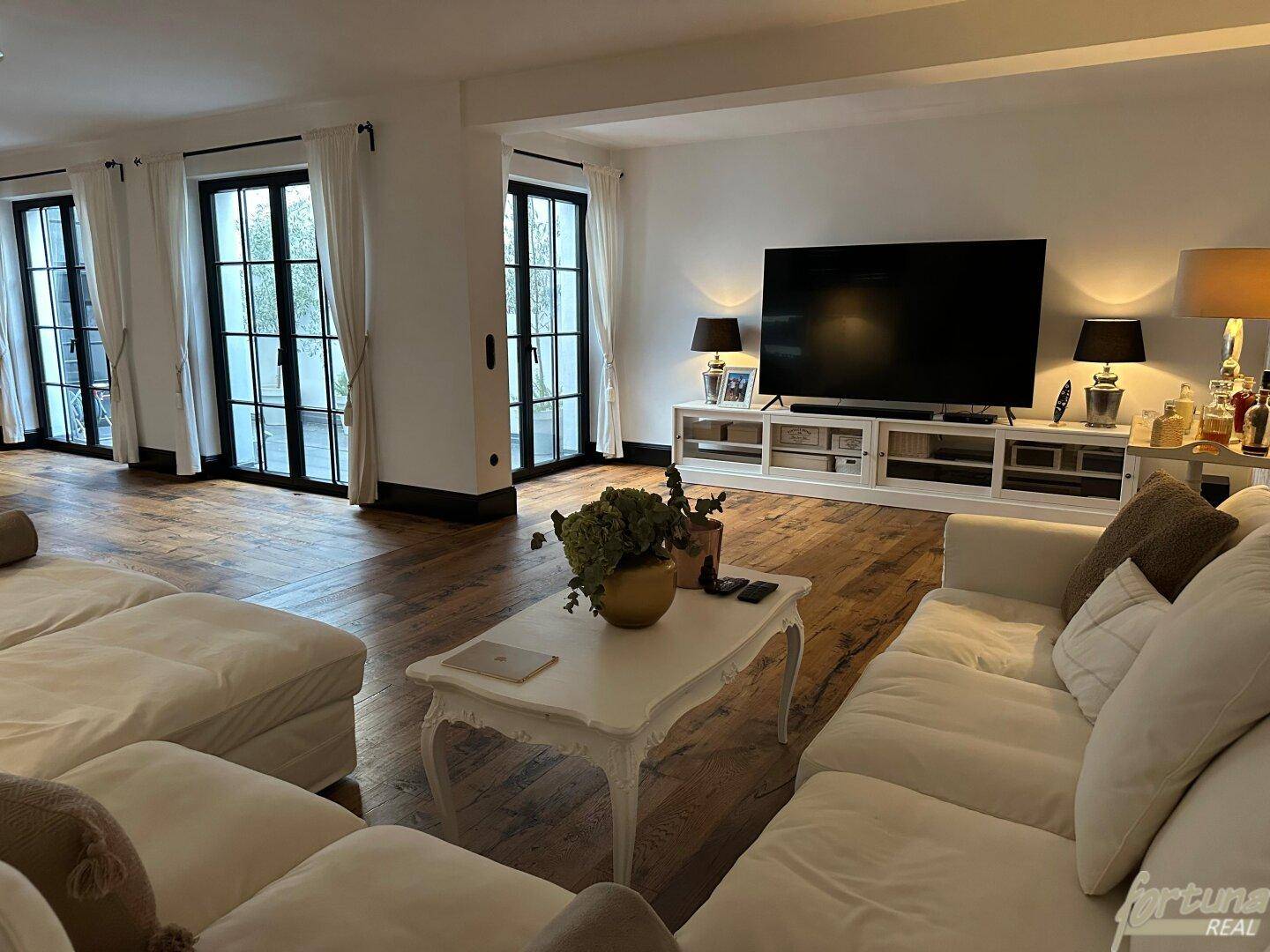 Helles Wohnzimmer mit bequemen Sofas, großem Fernseher und Zugang zu einem Außenbereich.