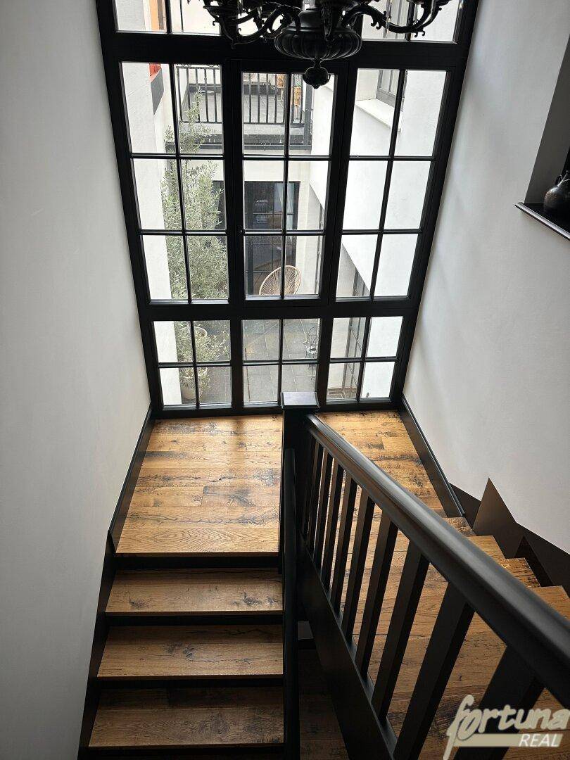 Elegantes Treppenhaus mit großem Fenster, das viel Licht hereinlässt und einen Blick nach draußen bietet.