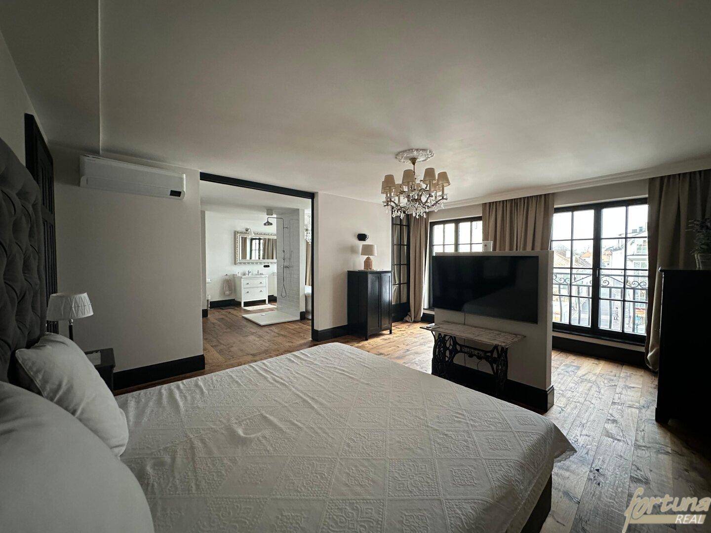 Komfortables Schlafzimmer mit großem Bett, Fernseher und direktem Zugang zu einem Badezimmer.