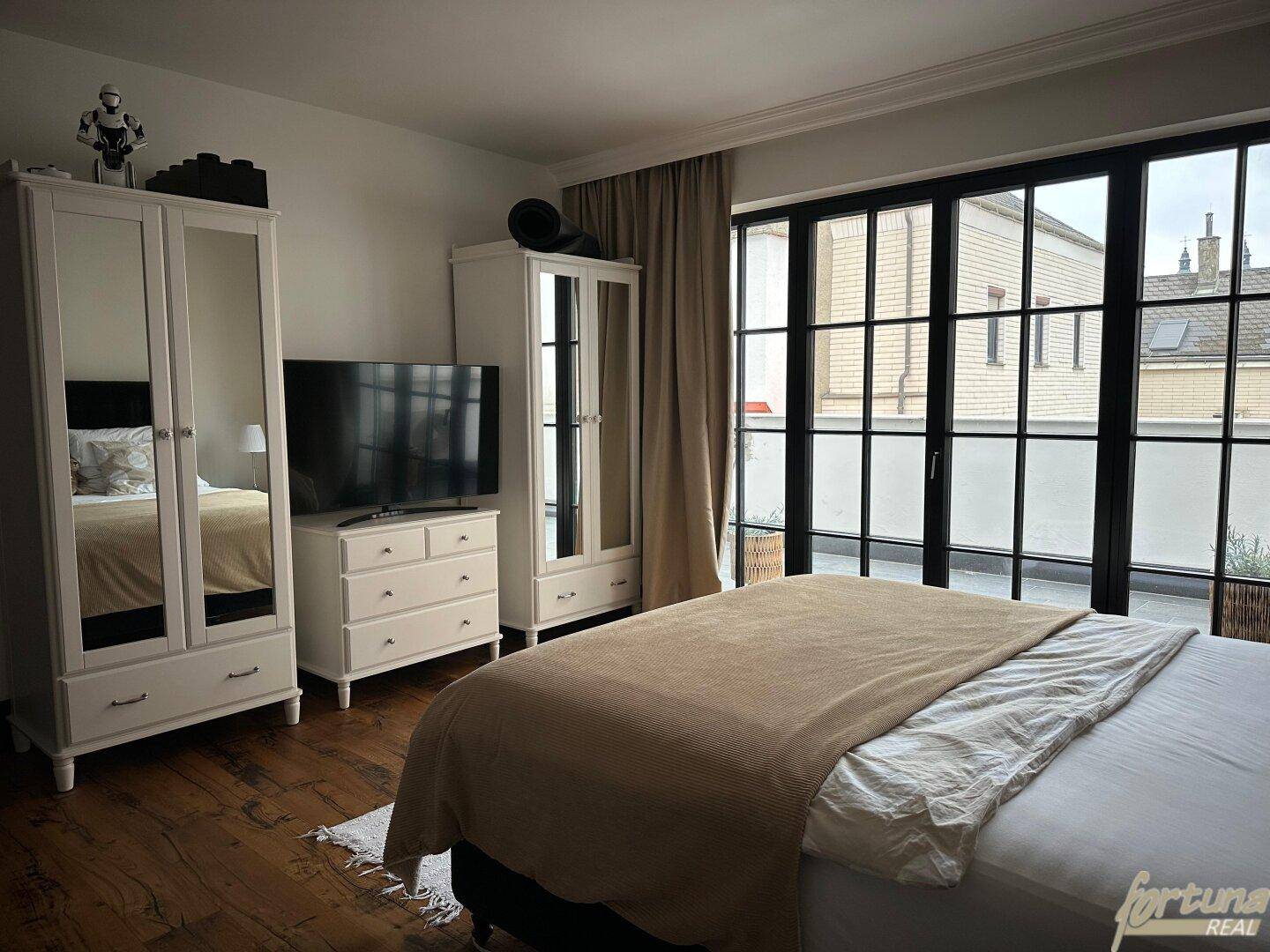 Helles Schlafzimmer mit großem Bett, Kleiderschränken und Zugang zu einem Balkon oder einer Terrasse.