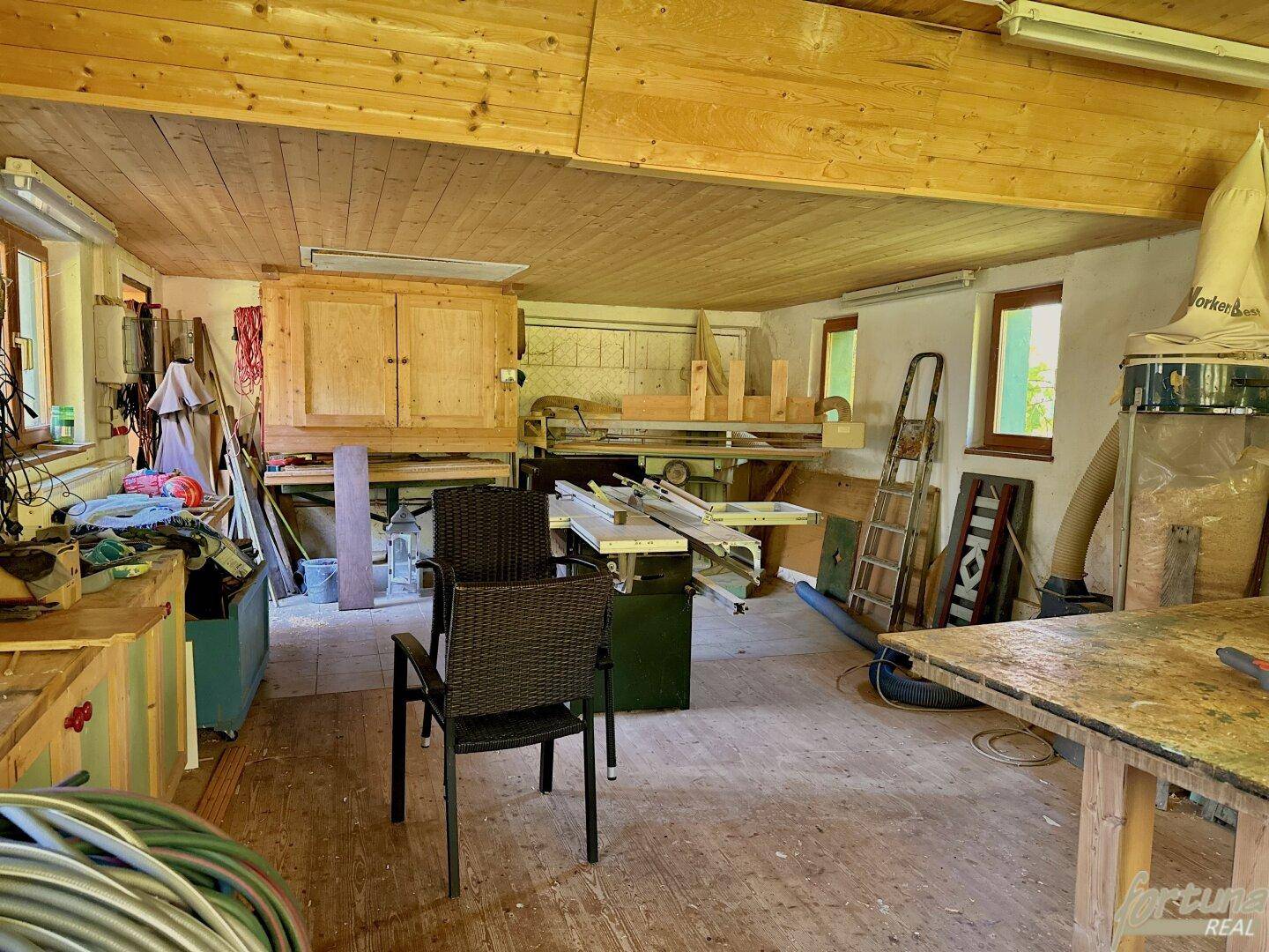 Geräumiger Hobbyraum mit Holzverkleidung, Werkbänken und natürlichem Lichteinfall durch Fenster.