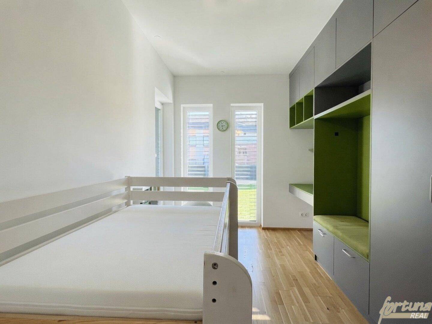 Helles Kinderzimmer mit Holzboden, integrierten Schränken und Blick in den Garten.