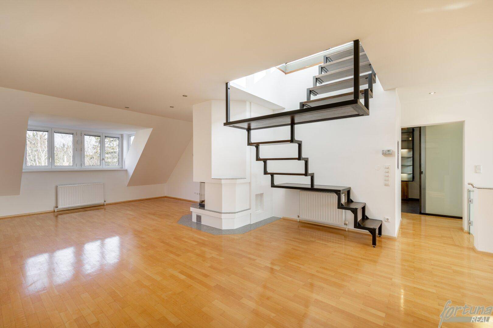 Geräumiges Wohnzimmer mit Holzboden, Kamin und offener Treppe zu einer oberen Etage.