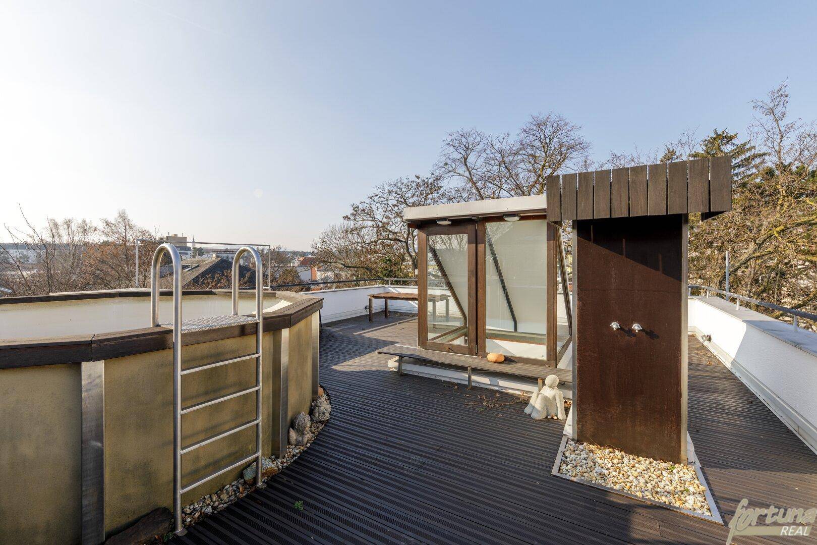 Dachterrasse mit Pool, Außendusche und Holzboden unter blauem Himmel.