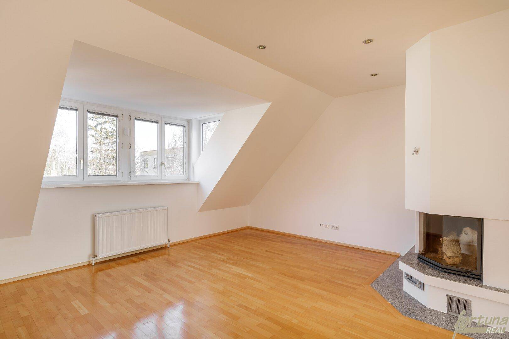 Helles Wohnzimmer mit Holzboden, Kamin und Dachschrägenfenstern, bereit zur Einrichtung.