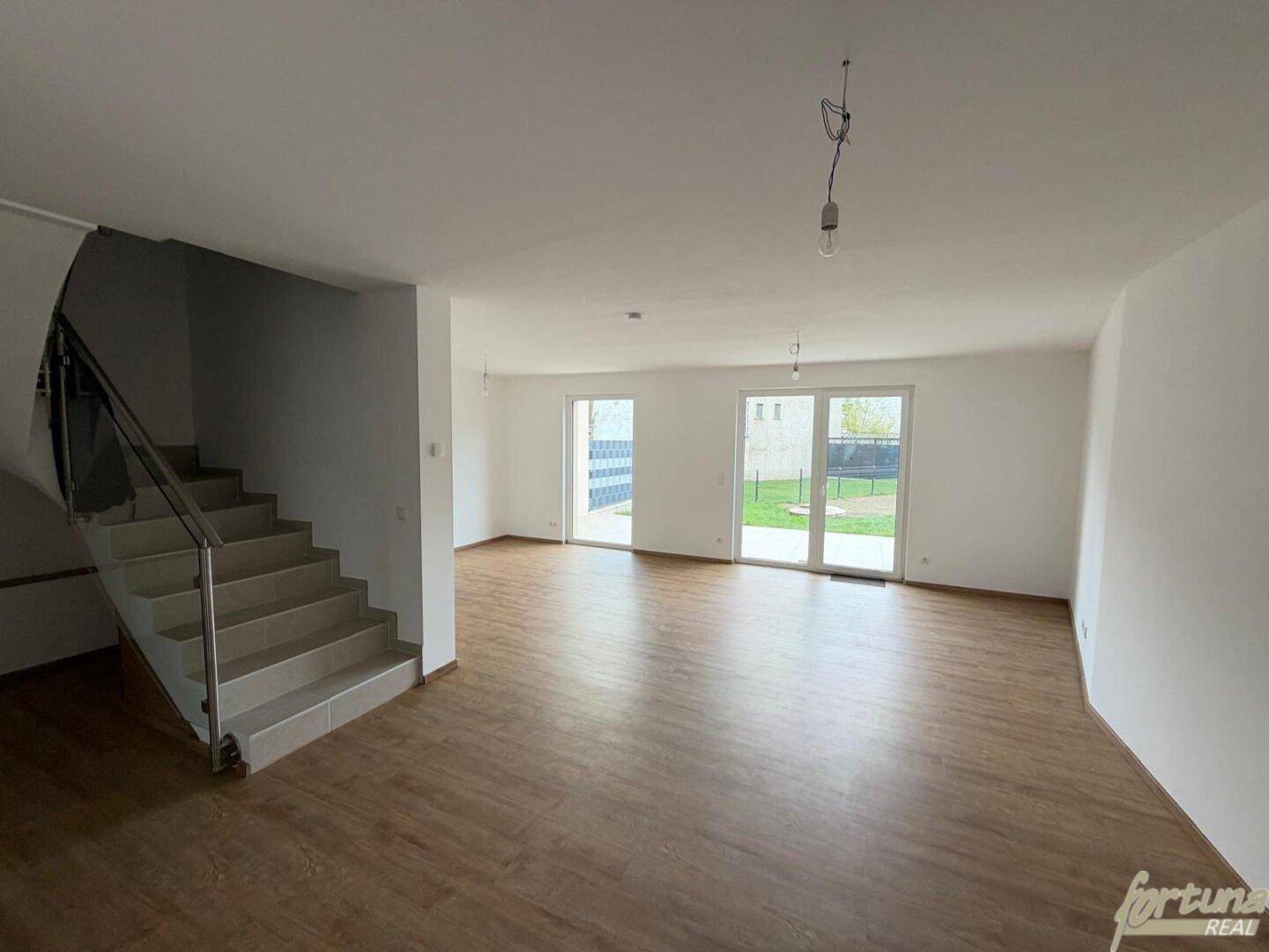 Geräumiges Wohnzimmer mit Laminatboden, Treppe und Zugang zum Garten durch große Türen.