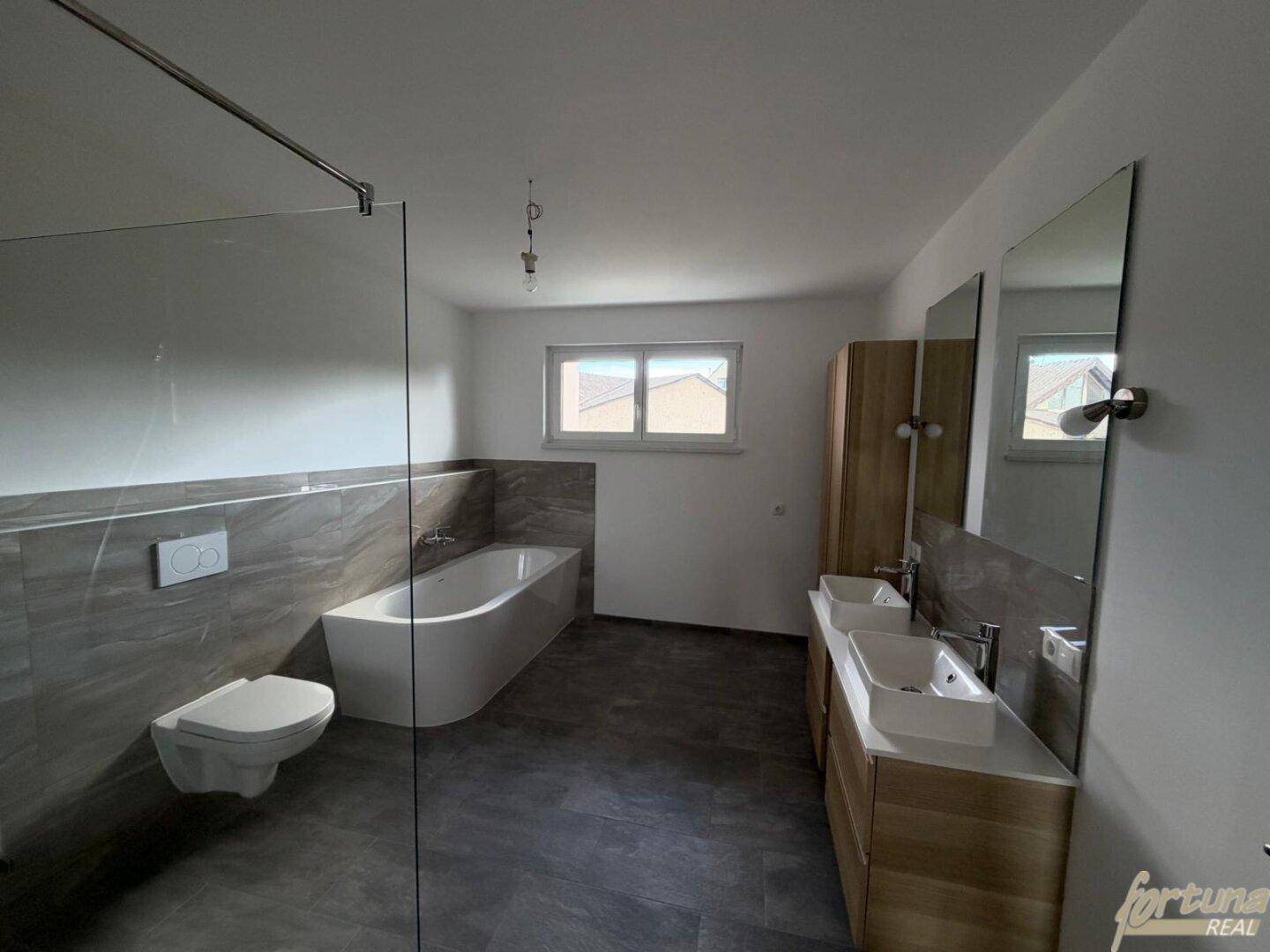 Modernes Badezimmer mit Badewanne, wandhängendem WC und großformatigen Fliesen.