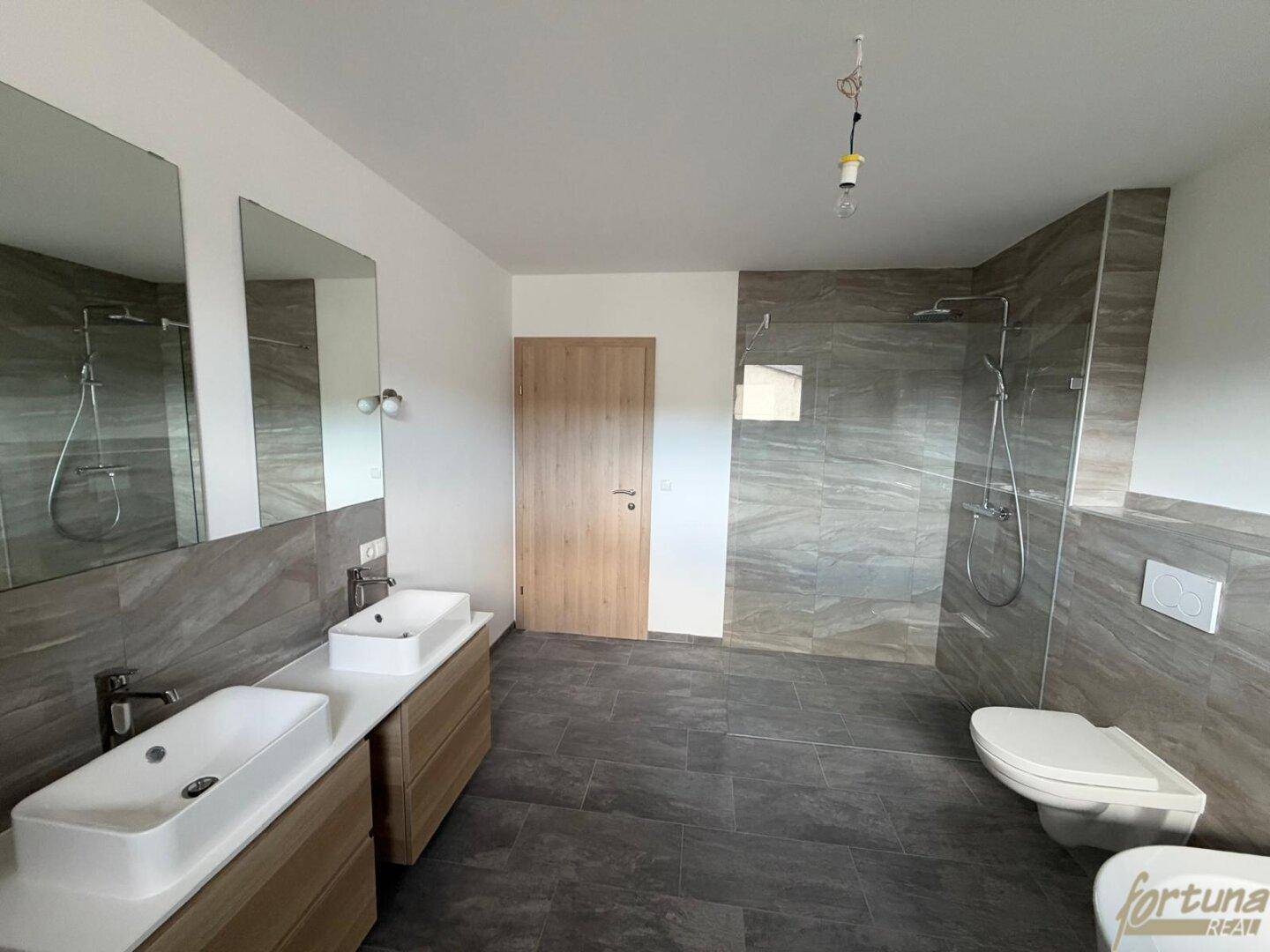 Geräumiges Badezimmer mit Doppelwaschbecken, großer begehbarer Dusche und modernen Fliesen.