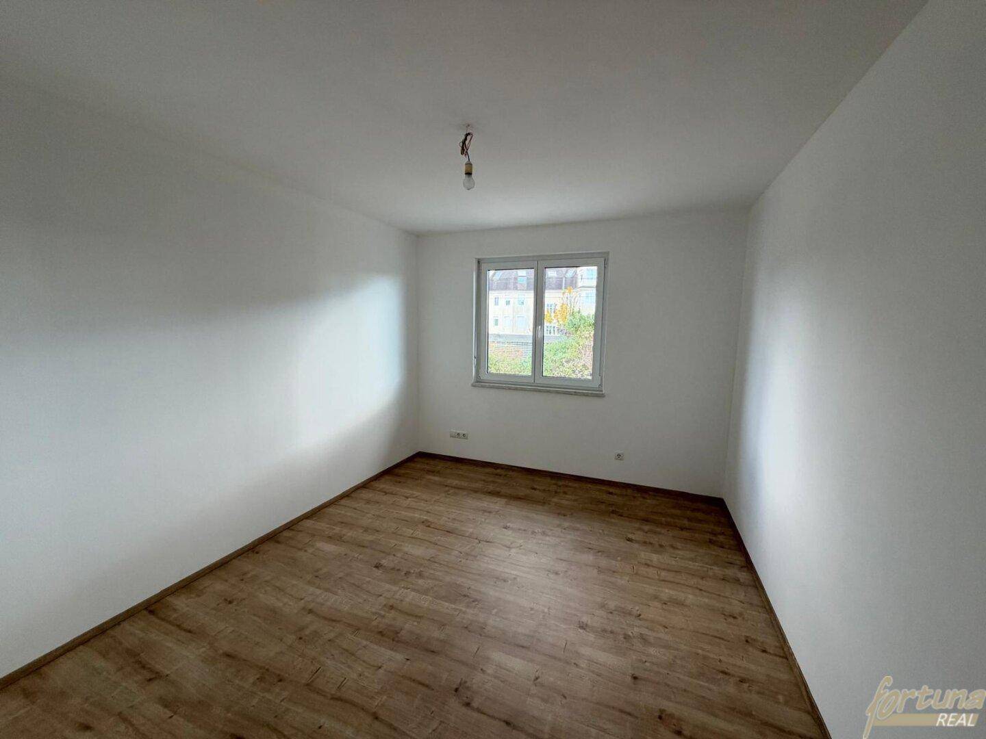 Geräumiges Schlafzimmer mit Laminatboden und Fenster, ideal für individuelle Einrichtung.
