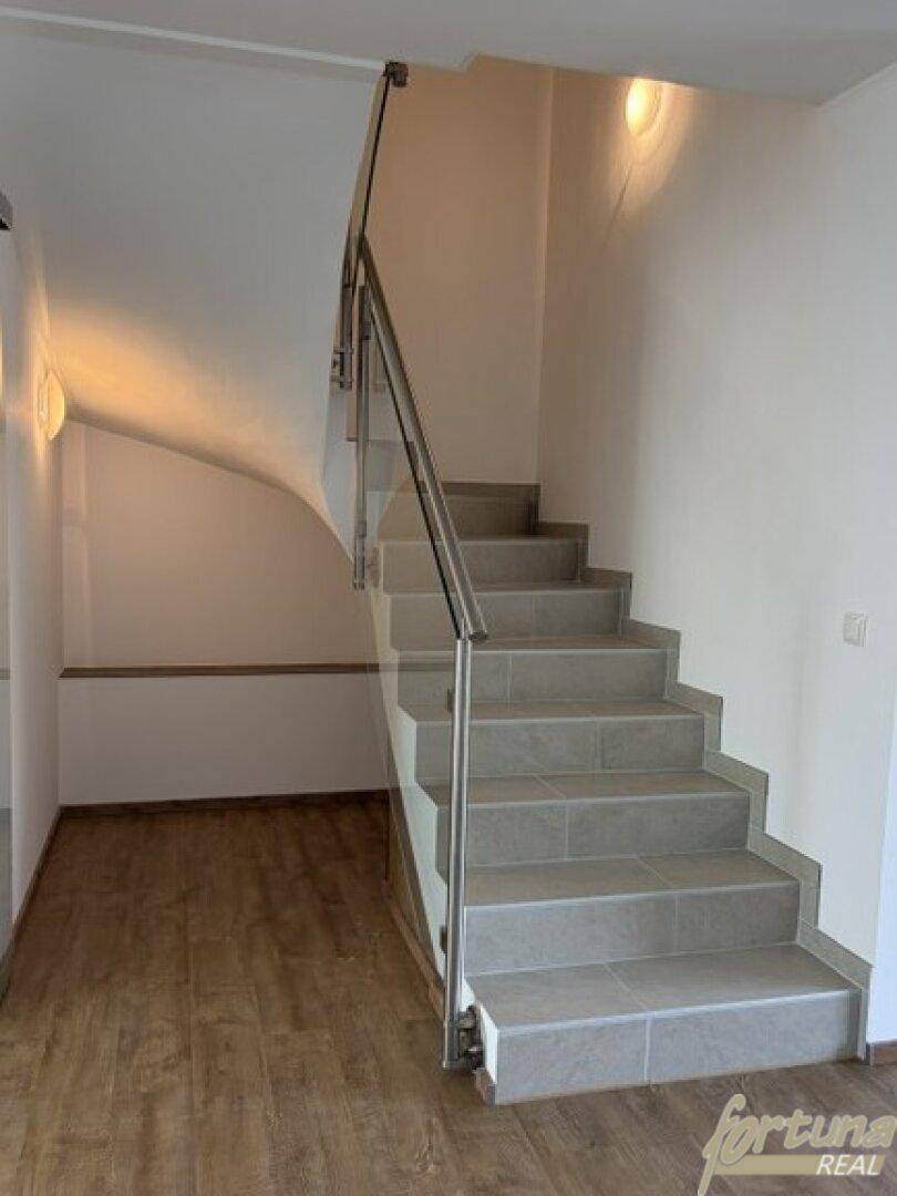 Heller Treppenaufgang mit Fliesenstufen und modernem Edelstahlgeländer.