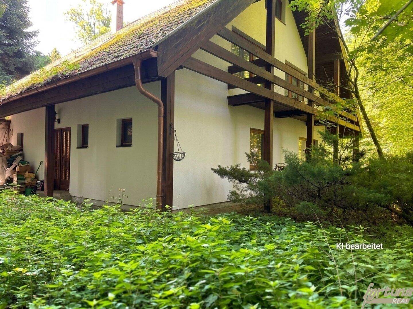 Rustikales Haus umgeben von dichtem Grün und Bäumen, mit einem Holzbalkon im oberen Stockwerk.
