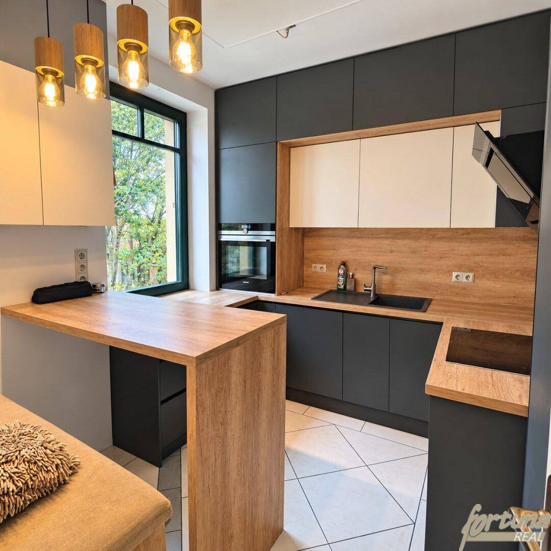 Moderne Küche mit grauen und weißen Schränken, Holzarbeitsplatten und integrierter Frühstücksbar.