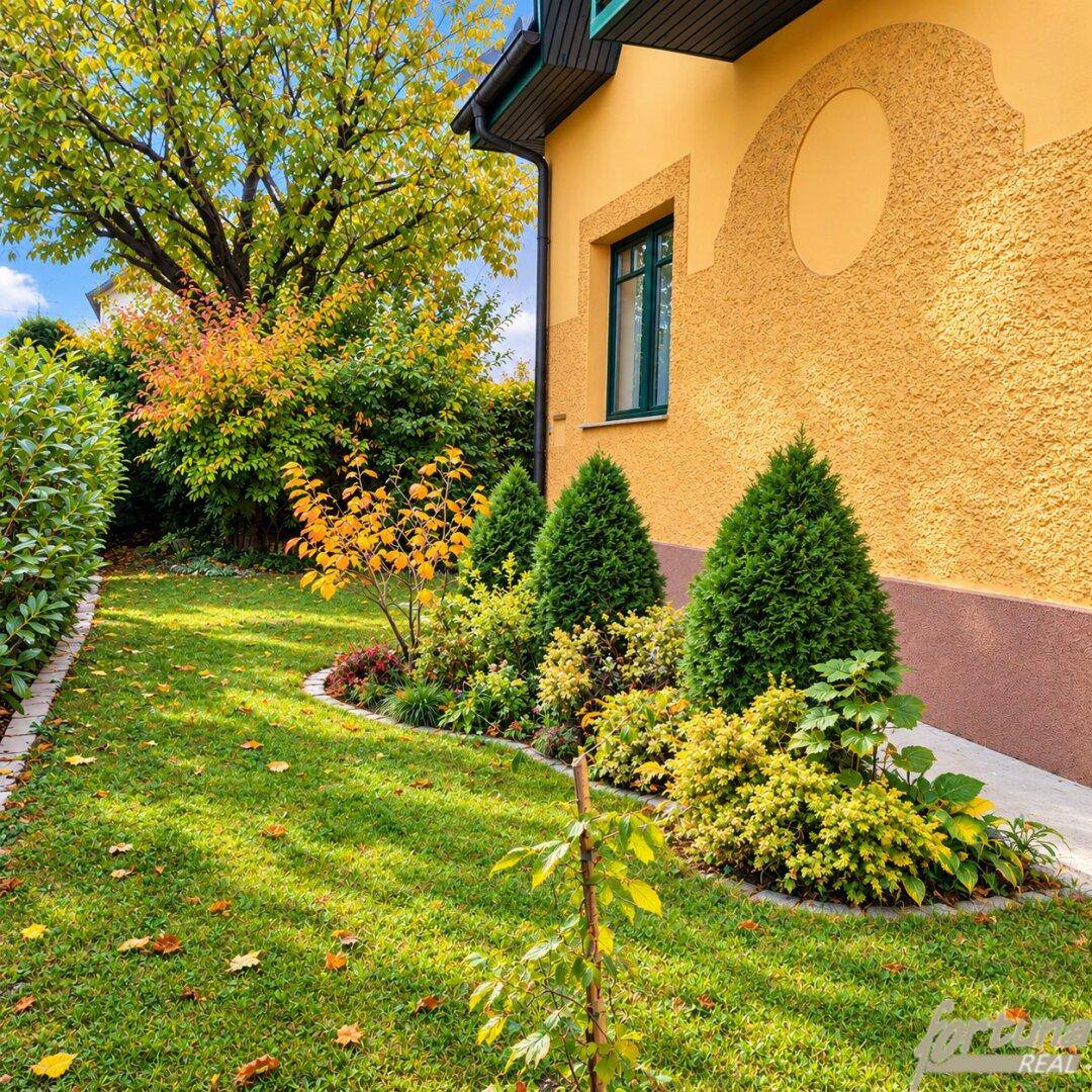Seitlicher Gartenbereich des Hauses mit gepflegten Sträuchern, Rasenfläche und Herbstbäumen.