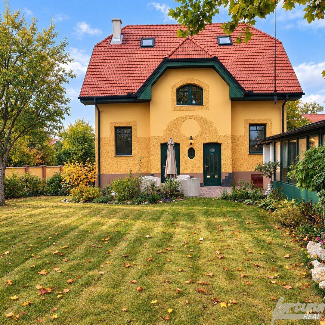 Charmantes gelbes Haus mit rotem Ziegeldach und gepflegtem Vorgarten unter blauem Himmel.