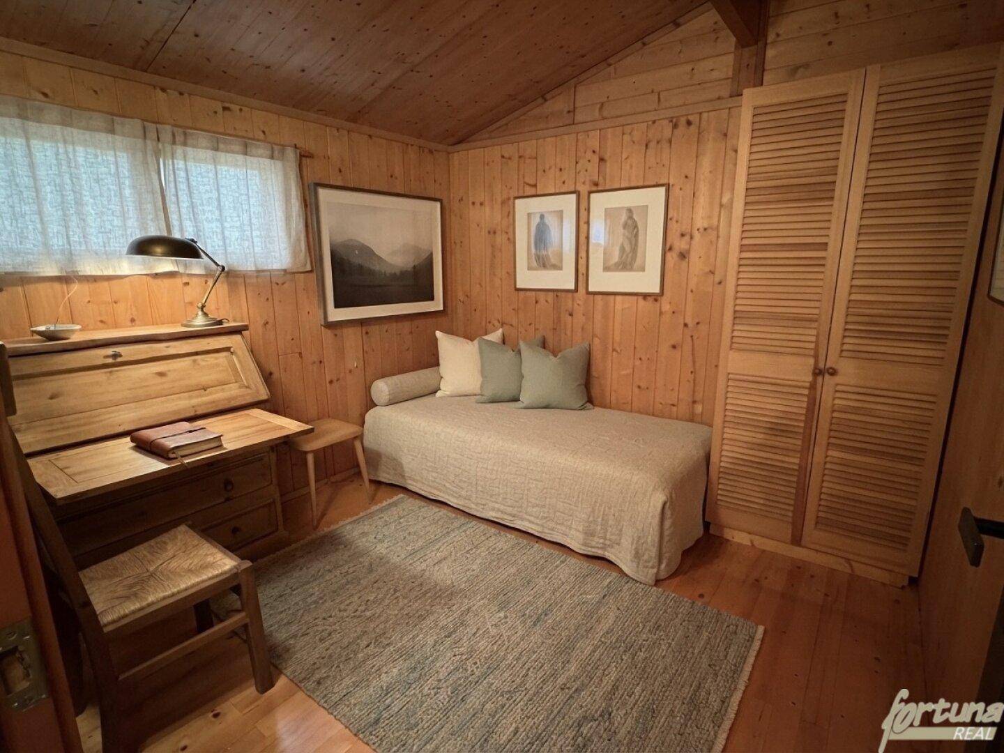 Helles Schlafzimmer mit Holztäfelung, Tagesbett und Schreibtisch, ideal als Gäste- oder Arbeitszimmer.