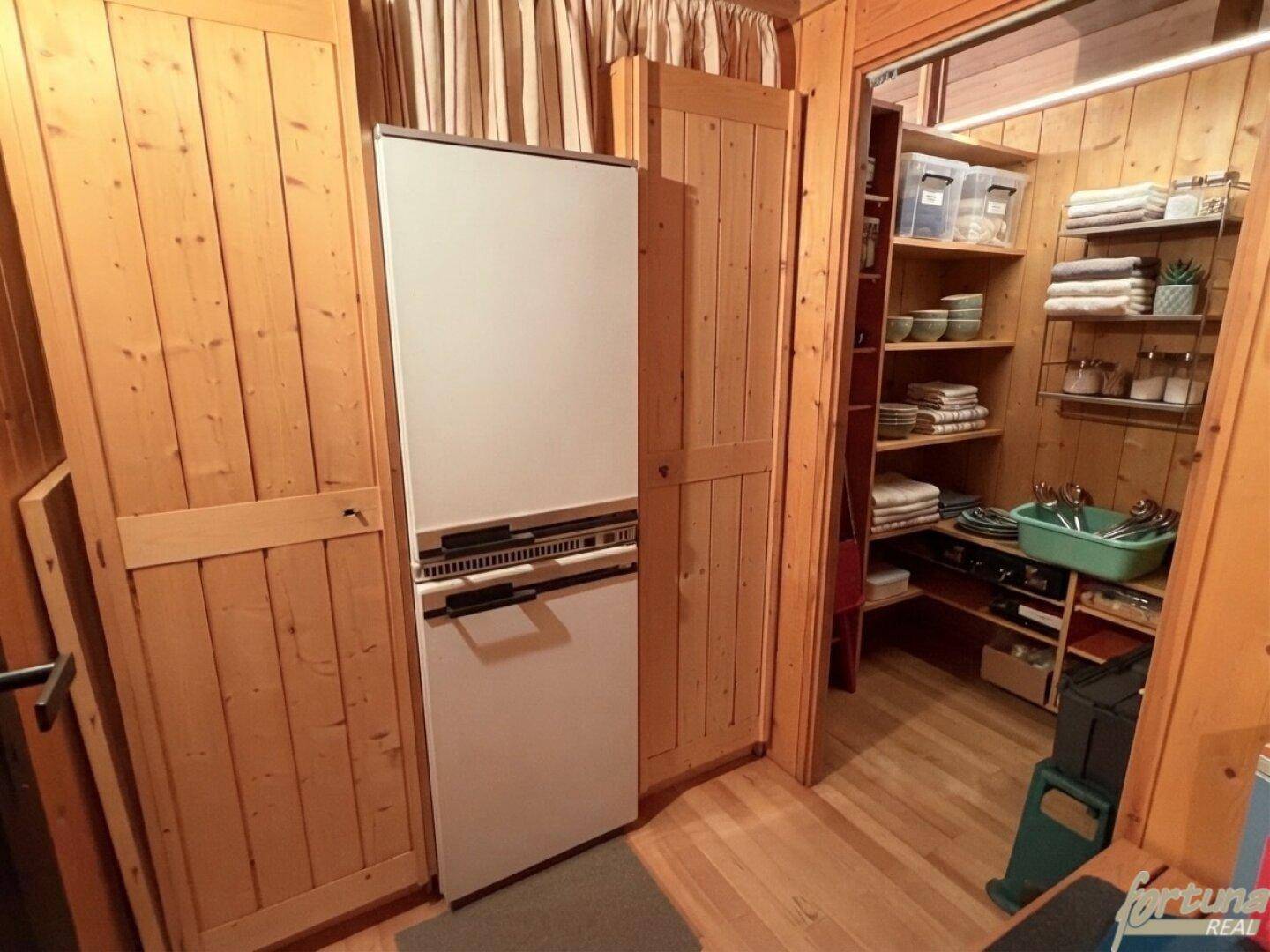 Praktischer Abstellraum mit Kühlschrank und Regalen für Vorräte, bietet viel Stauraum.