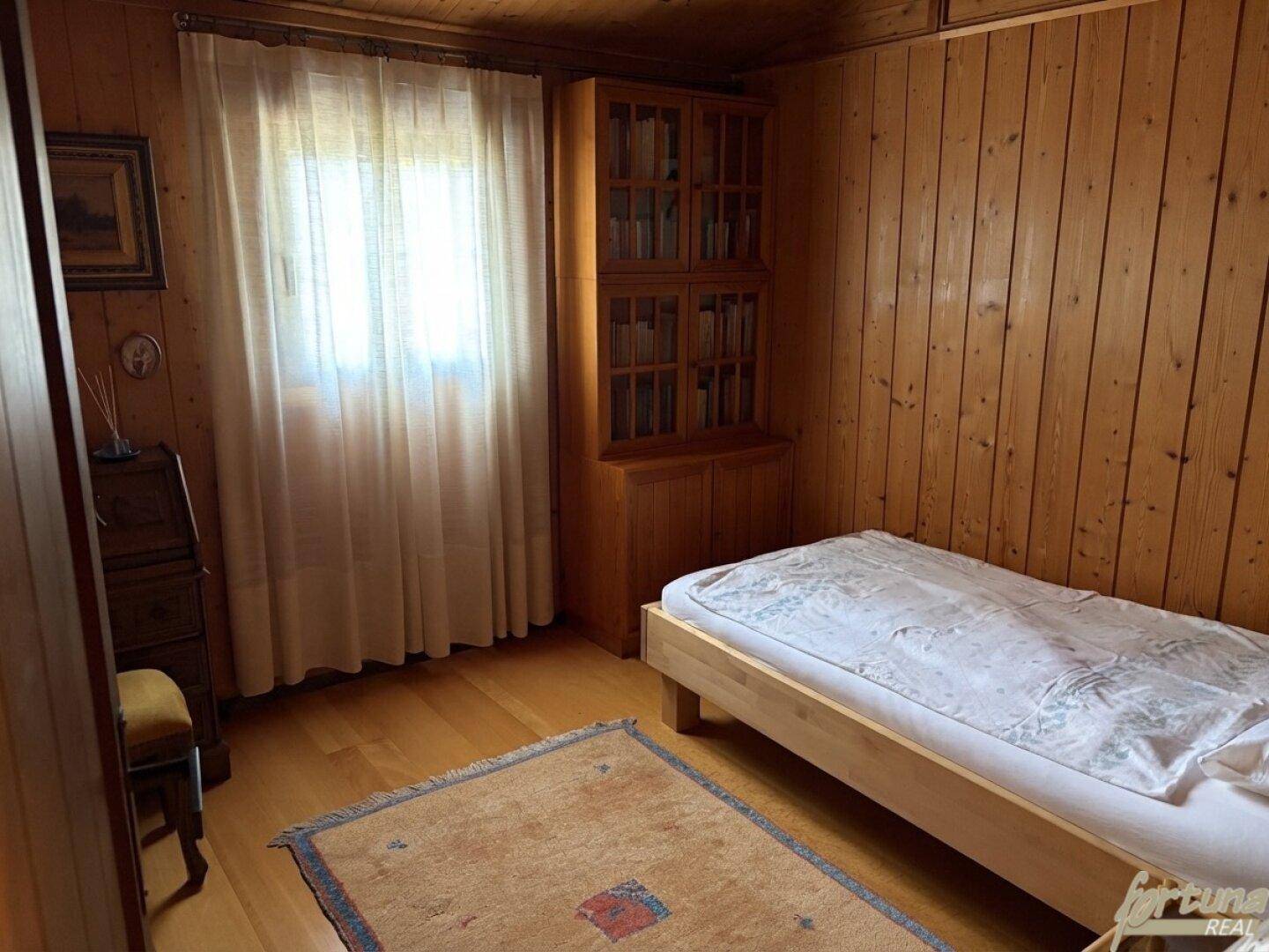 Helles Schlafzimmer mit Holztäfelung, Einzelbett und Bücherregal, bietet eine ruhige Atmosphäre.