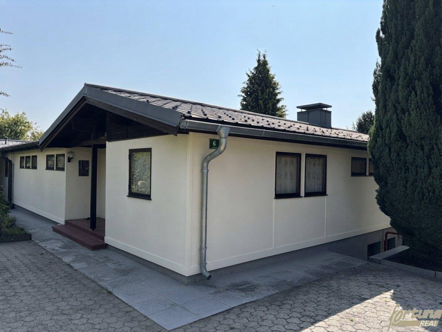 Einfamilienhaus mit heller Fassade, Satteldach und gepflasterter Zufahrt, in sonniger Lage.