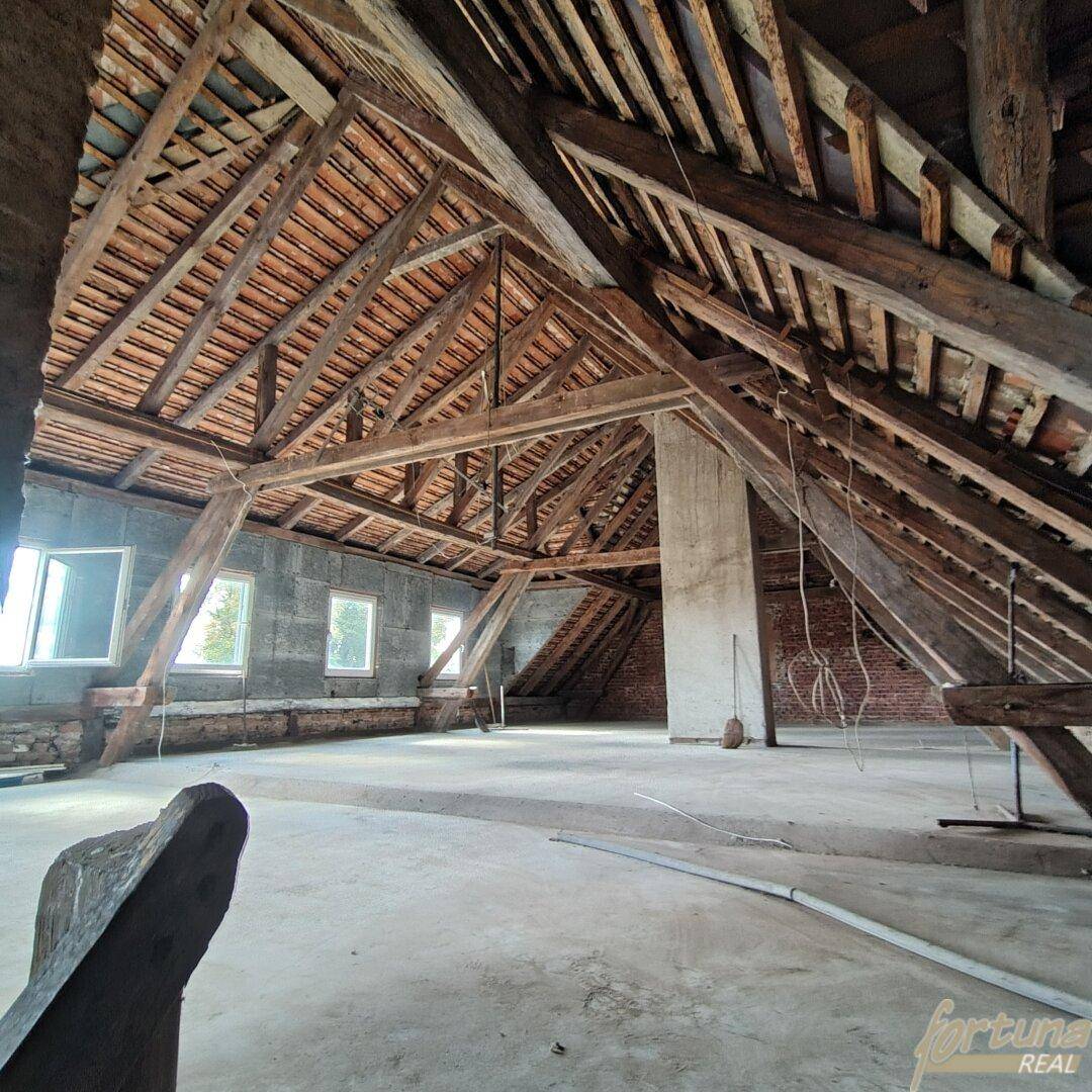 Geräumiger Dachboden mit sichtbaren Holzbalken und Fenstern, ideal für Ausbauprojekte.