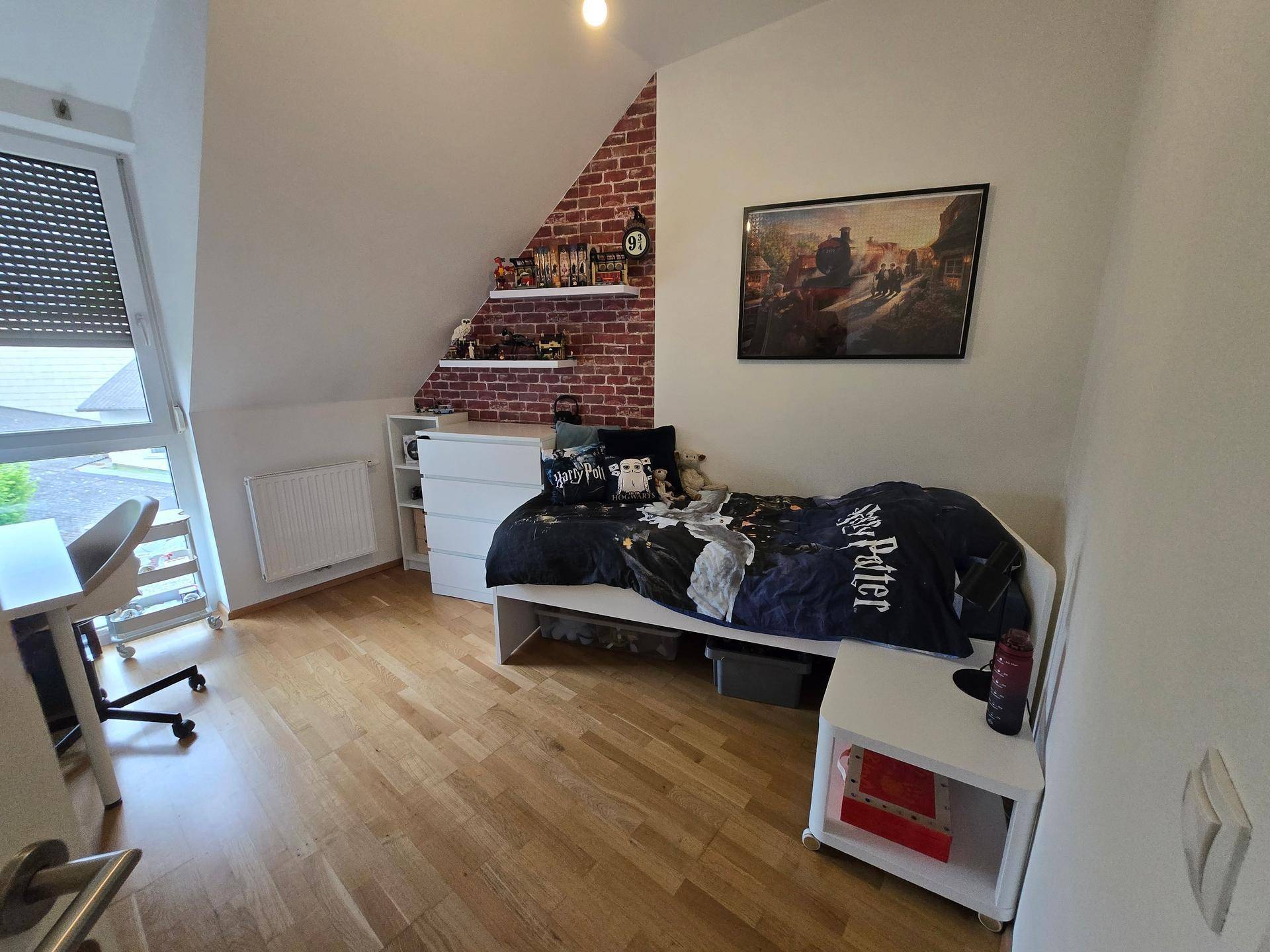 Kinderzimmer mit Holzboden, Dachschräge und einer dekorativen Ziegelwand als Akzent.