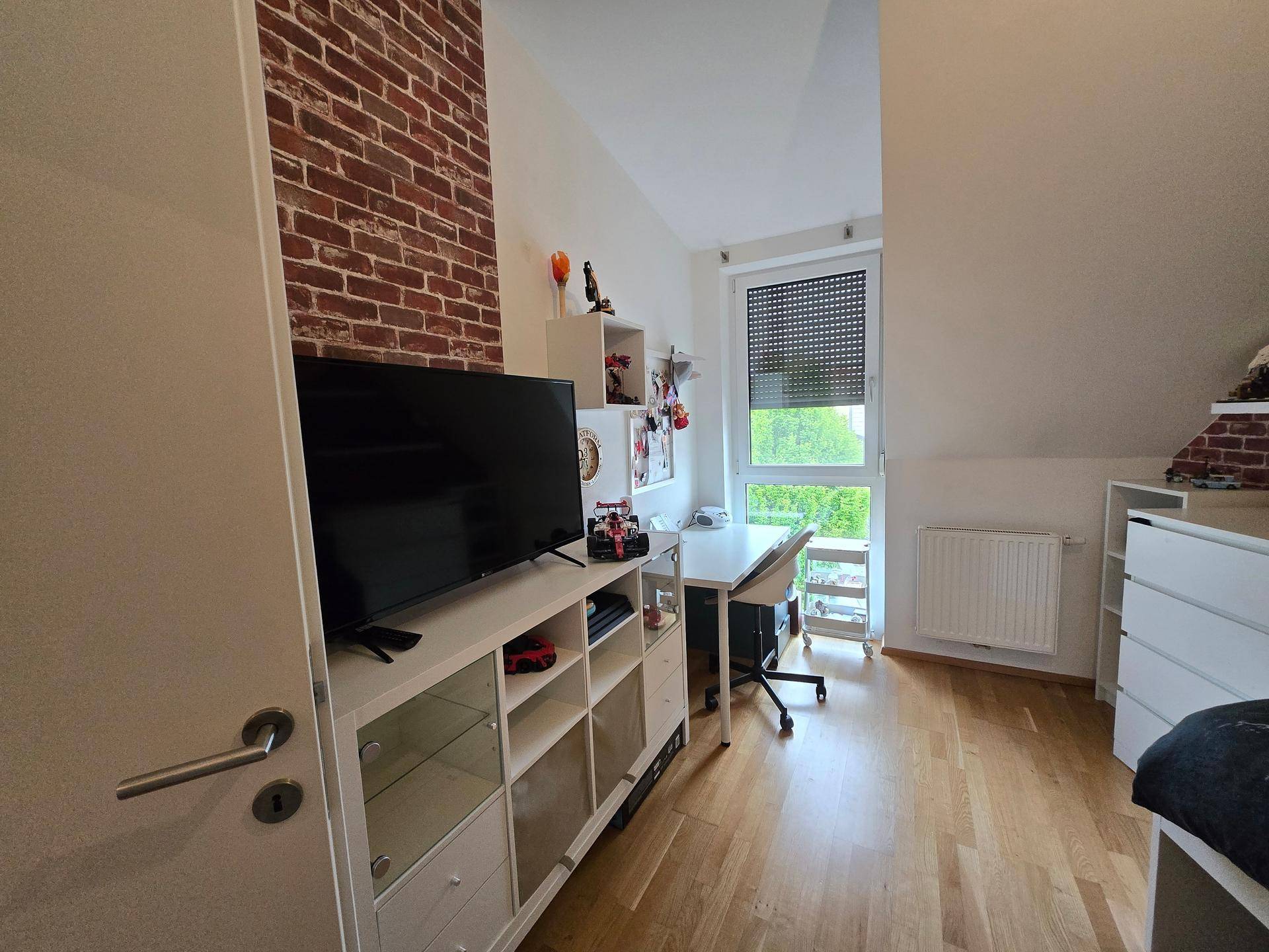 Helles Schlafzimmer mit Holzboden, Dachschräge und einem Fernseher auf einem Sideboard.