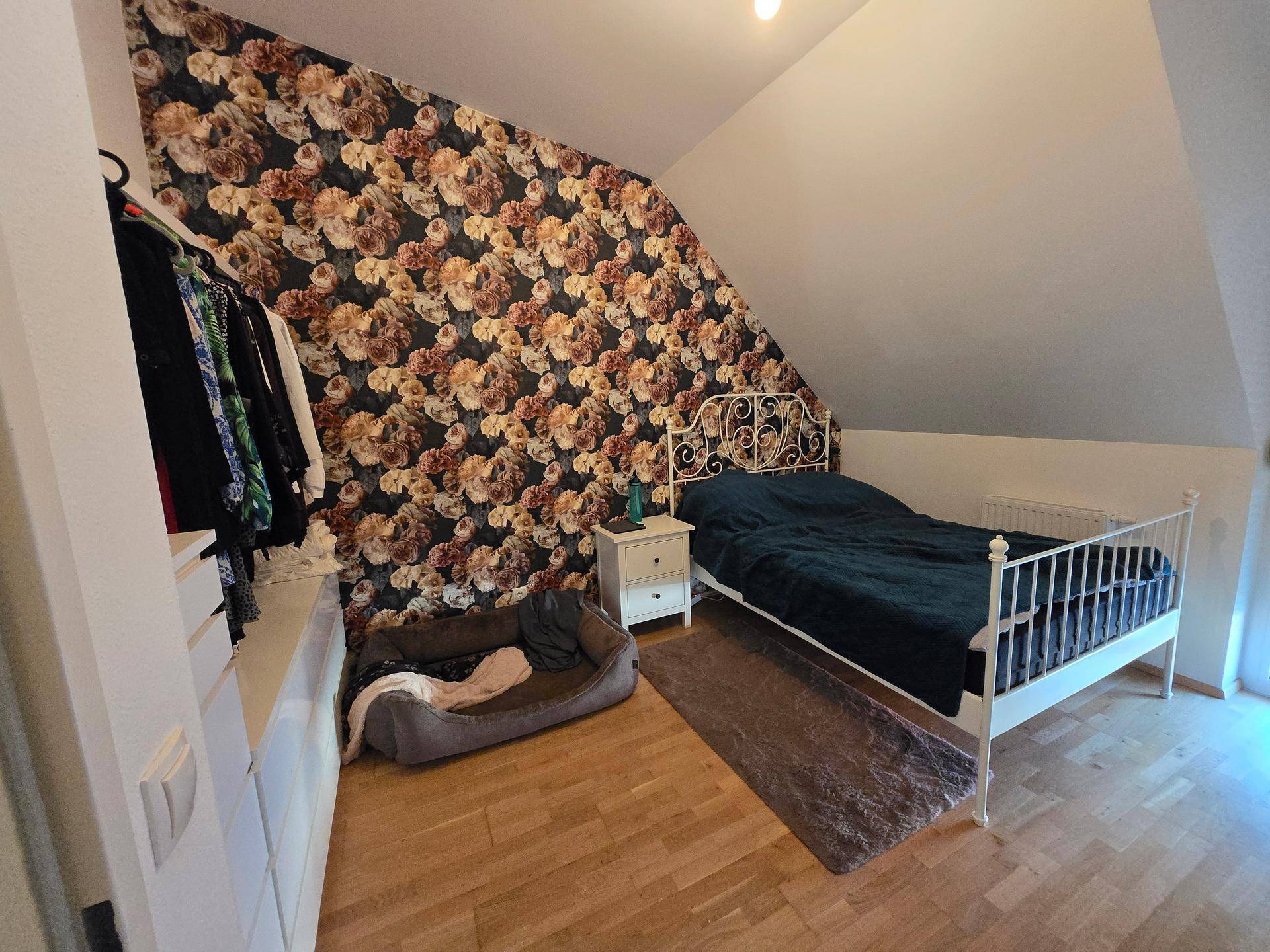 Gemütliches Schlafzimmer mit floraler Tapete, Holzboden und praktischem Kleiderschrank.