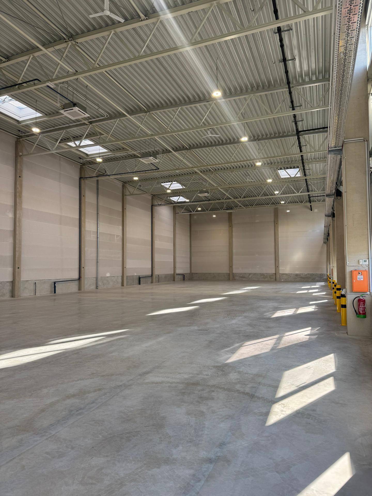 Große, unmöblierte Lagerhalle mit hohen Decken, Betonboden und Oberlichtern für zusätzliche Helligkeit.