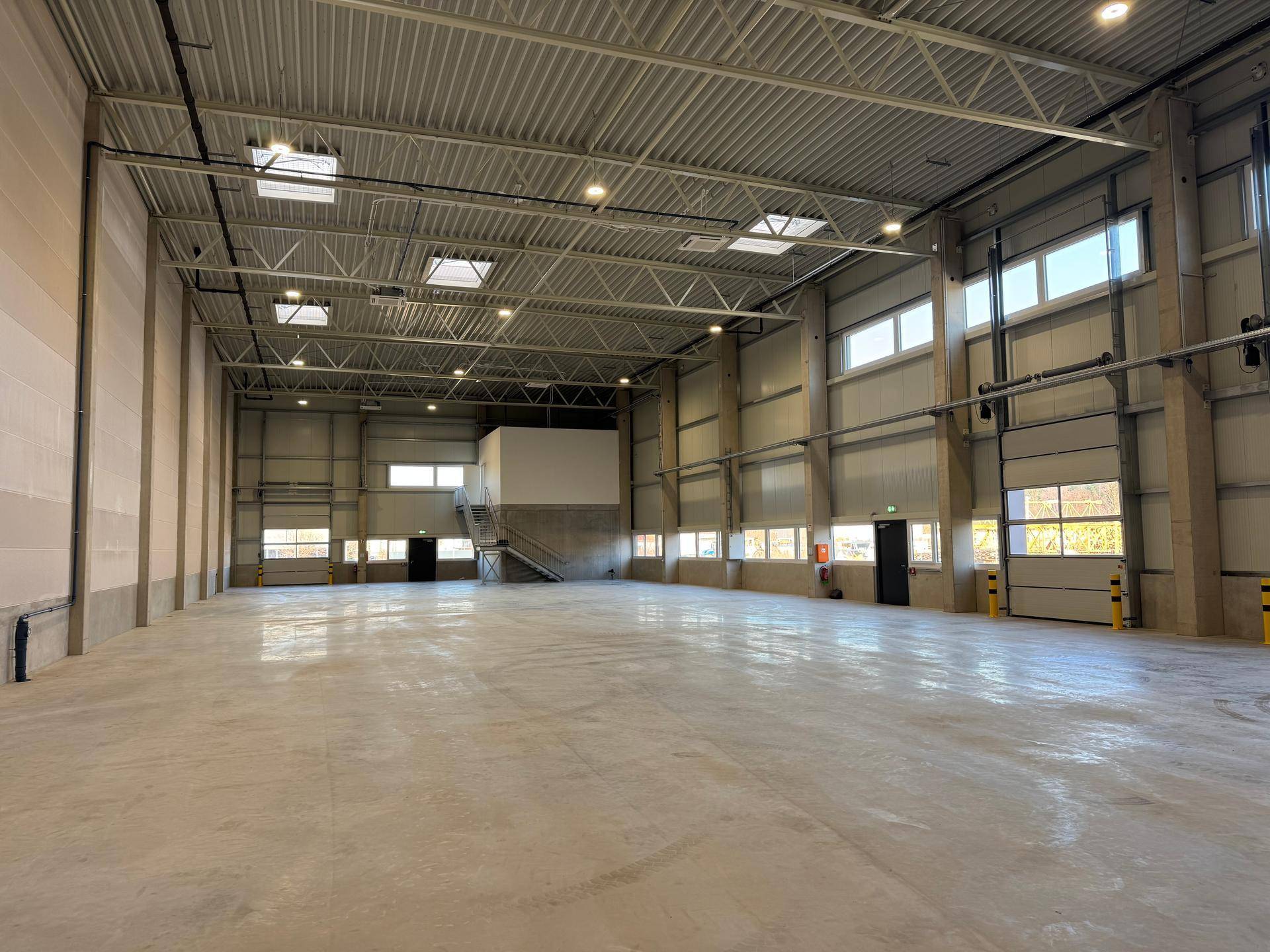 Geräumige, leere Lagerhalle mit hohen Decken, Betonboden und natürlichem Lichteinfall durch Fenster.