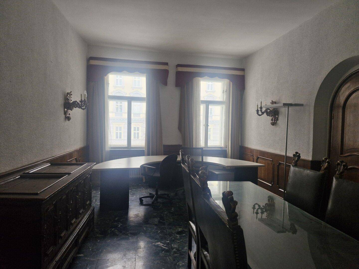 Geräumiges Büro mit dunklem Marmorboden, Holzvertäfelung und zwei großen Fenstern, die viel Tageslicht hereinlassen.
