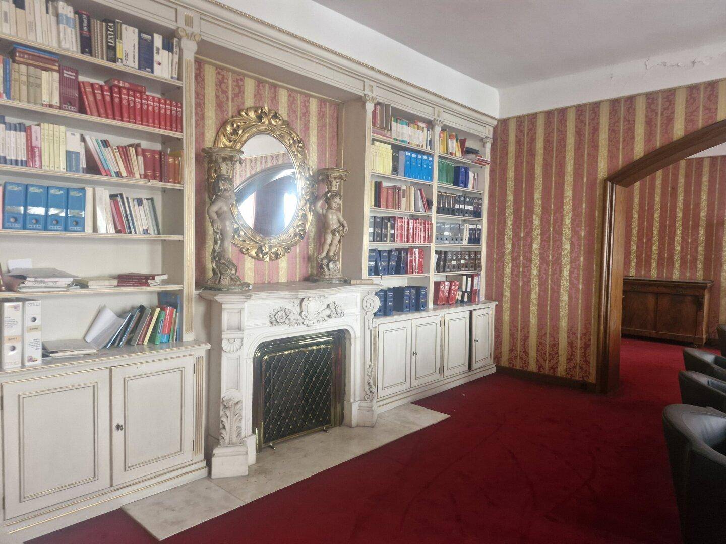Detailansicht des Wohnzimmers mit einem verzierten Kamin, eingebauten Bücherregalen und einem großen Spiegel.