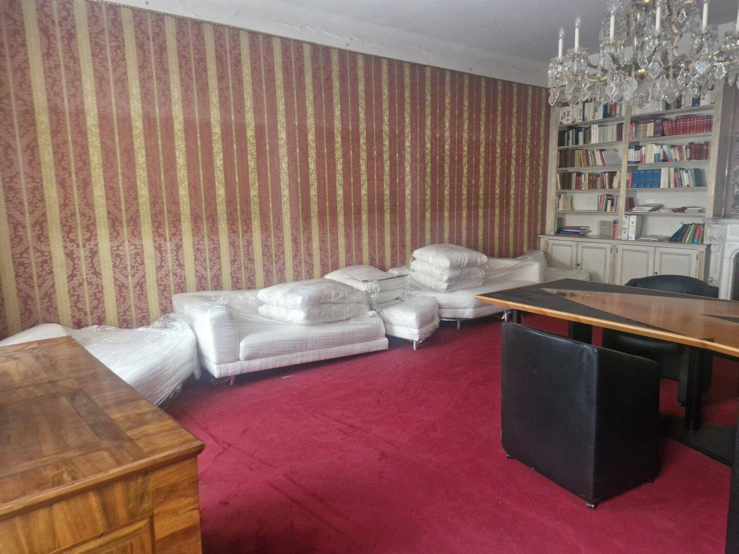 Geräumiges Wohnzimmer mit rotem Teppichboden und mehreren in Folie verpackten Sofas, bereit zur Einrichtung.