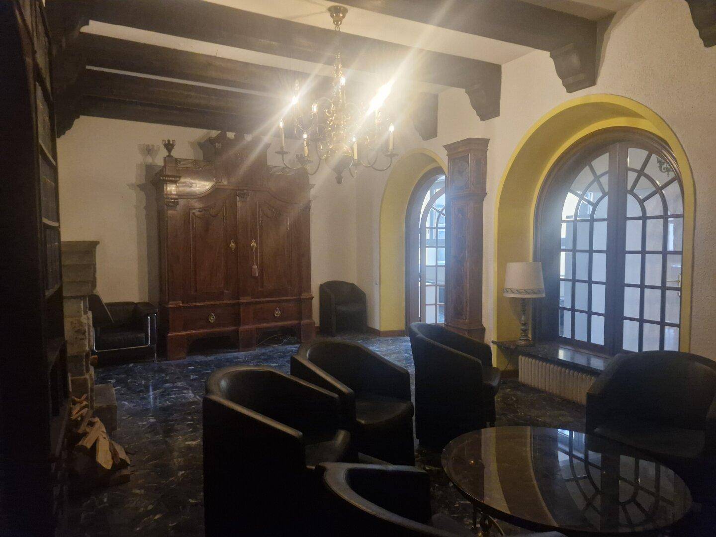 Wohnzimmer mit dunklem Marmorboden, einem Kronleuchter und großen Fenstern mit Rundbögen, die viel Licht spenden.