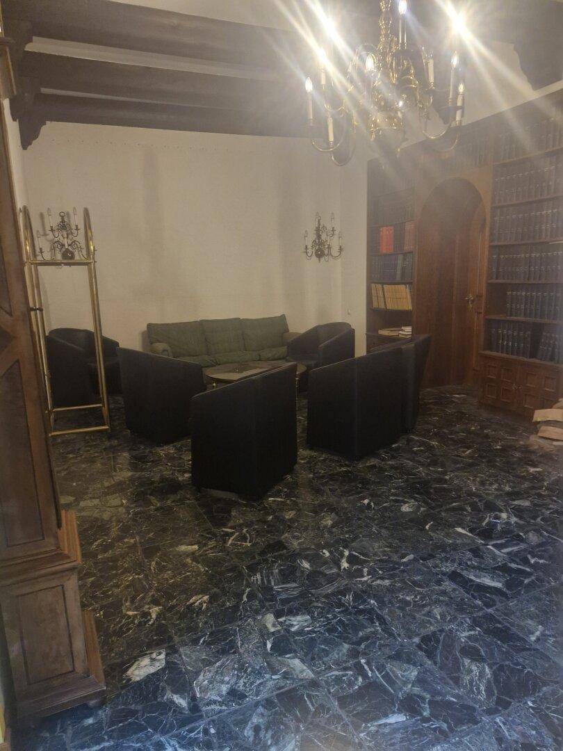 Wohnzimmer mit dunklem Marmorboden, einem Sofa und mehreren Sesseln, beleuchtet von einem Kronleuchter.