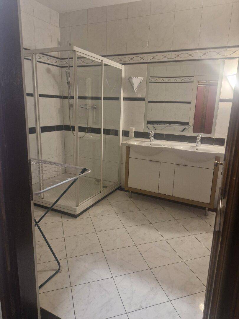 Badezimmer mit weißen Fliesen, einer Duschkabine und einem Doppelwaschbecken mit großem Spiegel.