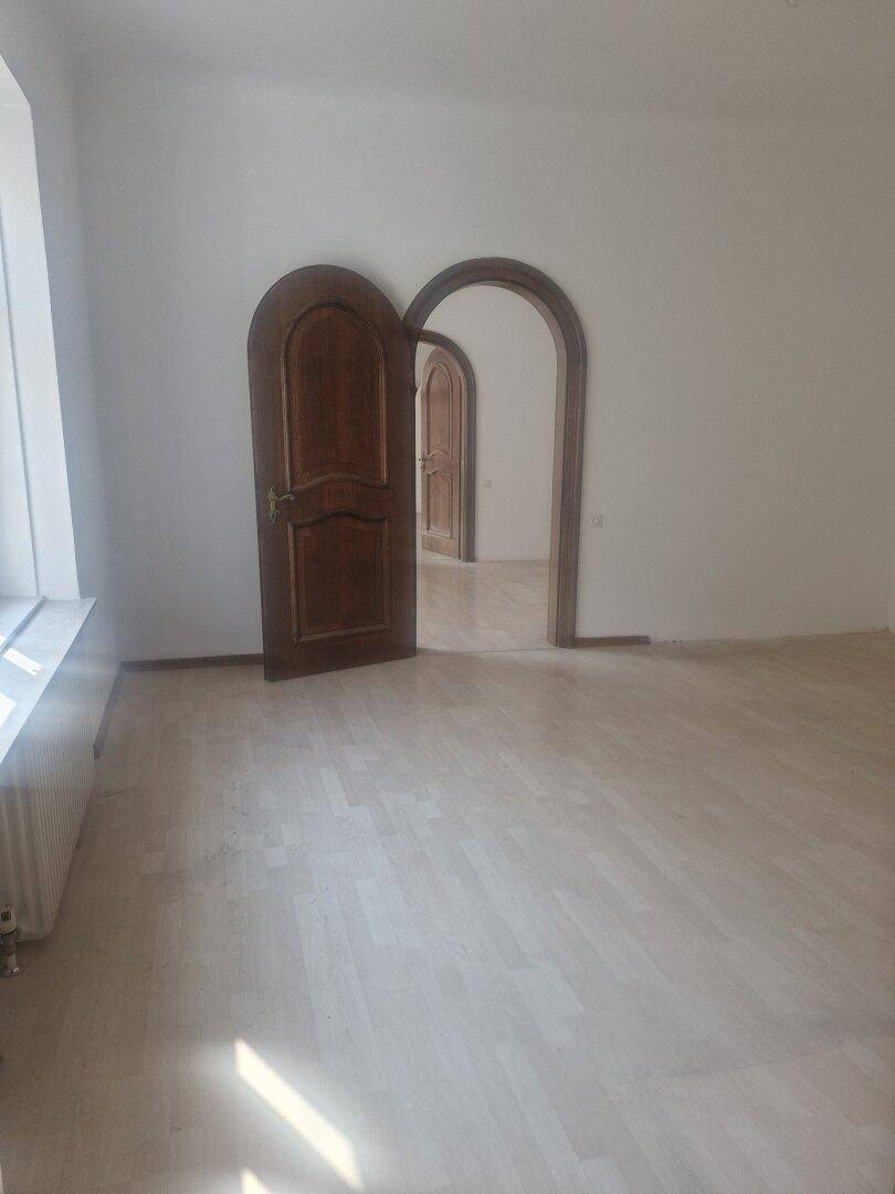 Geräumiger, unmöblierter Raum mit hellem Laminatboden und einer Reihe von Rundbogen-Türen.