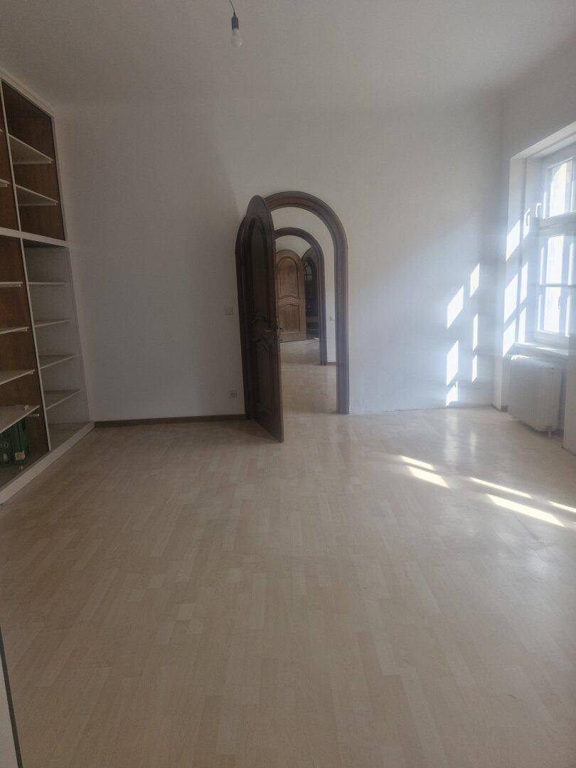 Heller Raum mit eingebauten Regalen, Laminatboden und einer Reihe von Rundbogen-Türen im Hintergrund.