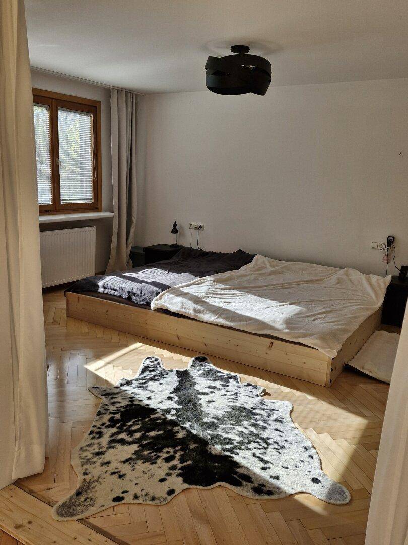 Helles Schlafzimmer mit Holzbettrahmen, Fischgrätparkett und dekorativem Kuhfellteppich.